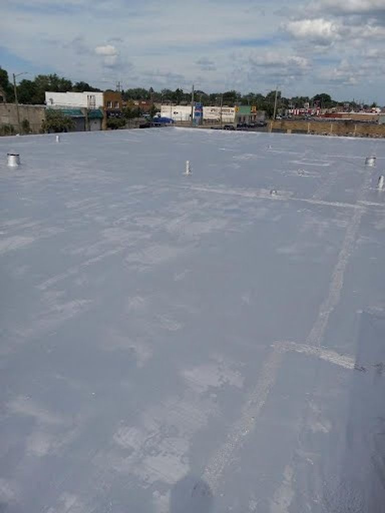 Silver-coated flat roof on a commercial building, with roof drains and vents