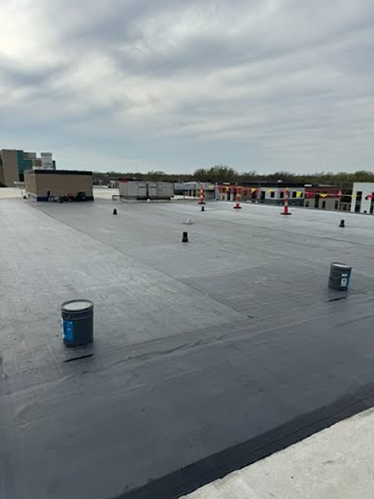 Black membrane being installed on a large commercial flat roof, with adhesive buckets on the deck