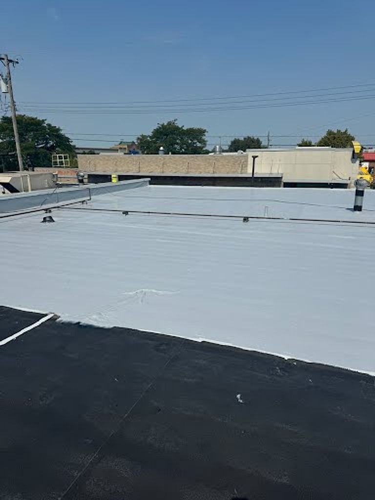 White roof coating being applied over a black flat roof on a commercial building