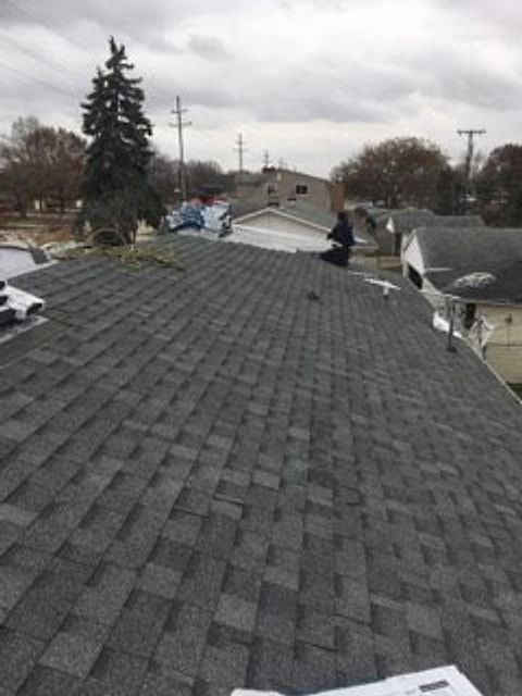 Roofer working on a dark gray architectural shingle roof in a residential neighborhood
