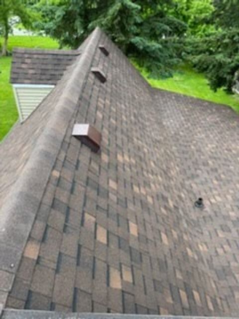 Shingle roof ridge with roof vents on a house surrounded by trees